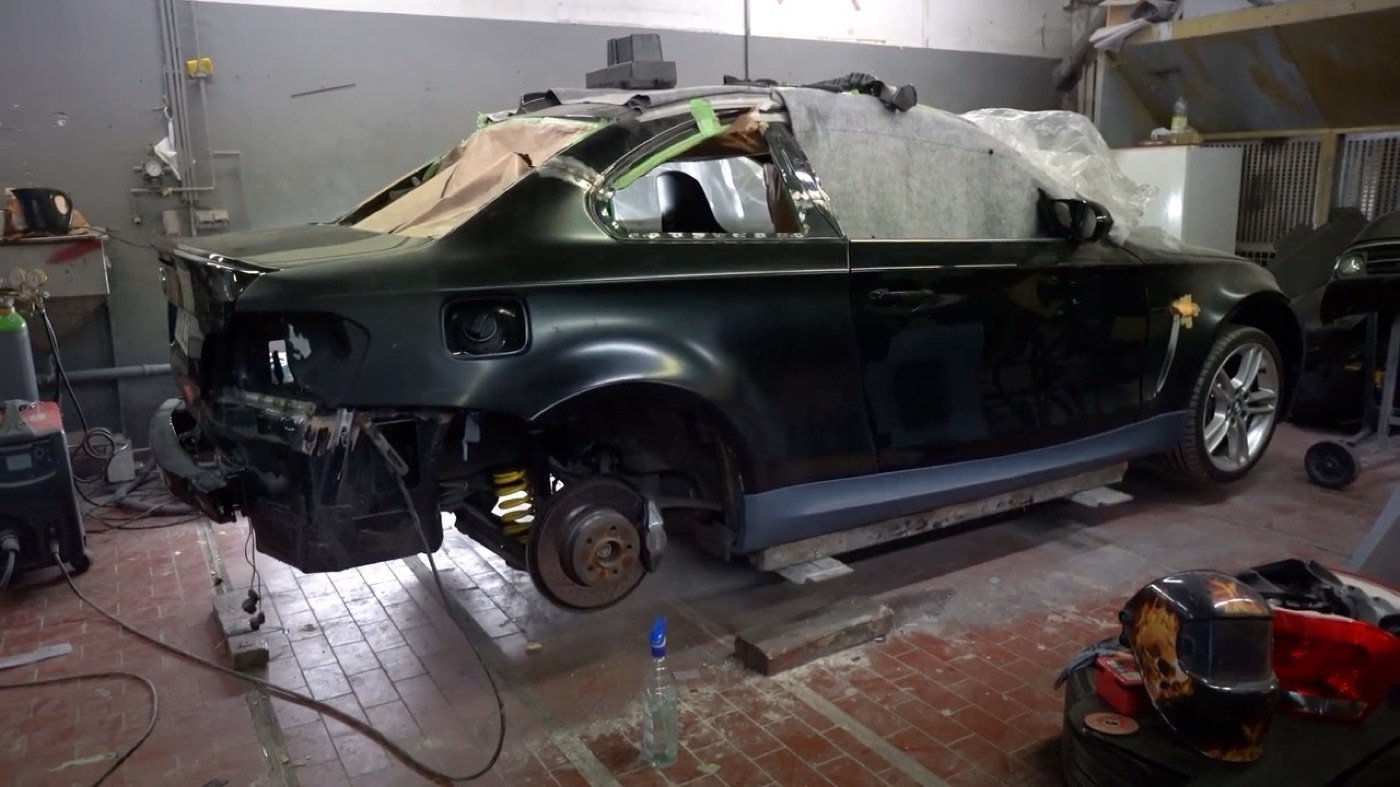 BMW 1er in der Werkstatt auf einer Hebebühne, Karosserie in Grundierung, umgeben von Werkzeug